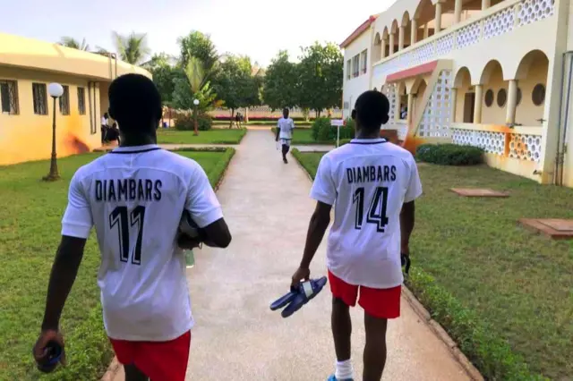 Deux joueurs vêtus de maillot blanc et short rouge marchent en direction du terrain.